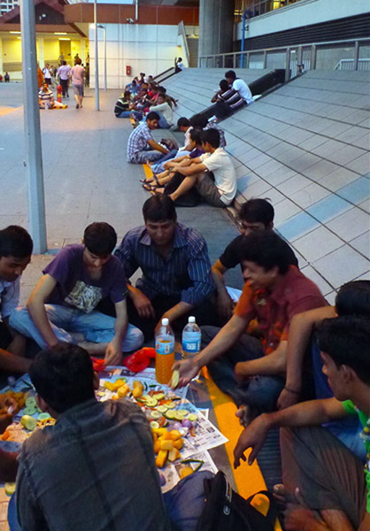 Bangladeshi Muslim migrant men breaking fast along a path to Boon Lay MRT station while commuters continue their journey from work. (Photo: Junjia Ye)