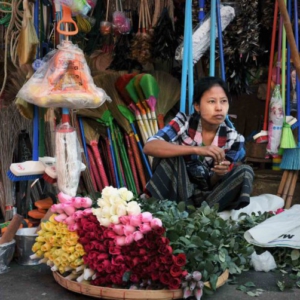 Fresh roses for sale from a flat woven bamboo receptacle on the sidewalk in front of a stall with assorted household goods. (Photo: Naomi Hellmann)