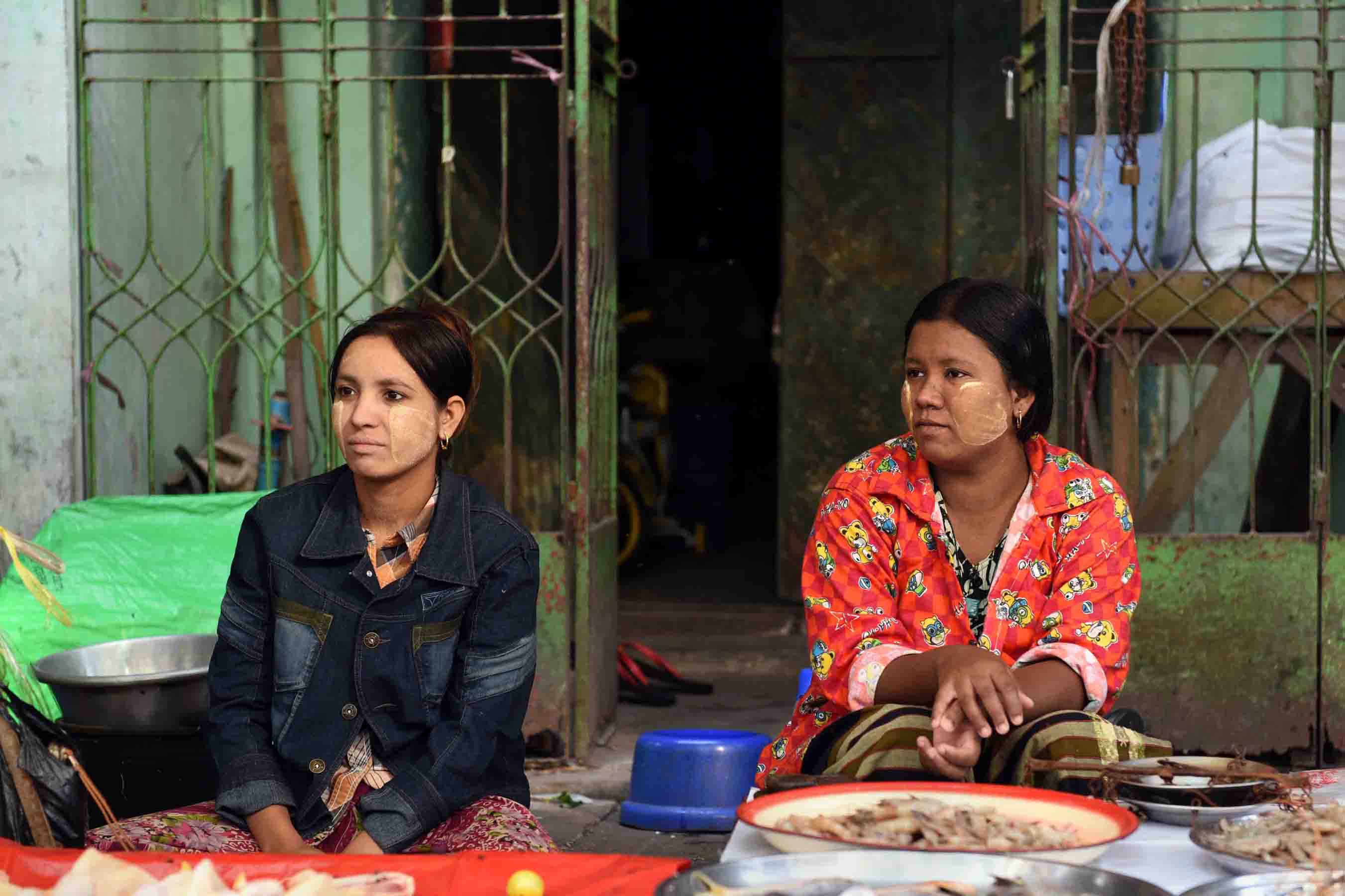 A pair of young fish mongers wearing thanaka waiting for customers. (Photo: Naomi Hellmann)
